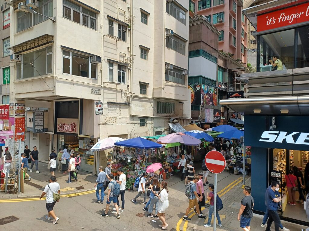 People walking beside market stalls on Tai Yuen Street in Wan Chai, photographed in June 2023