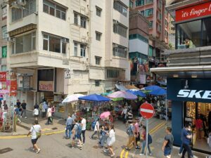 People walking beside market stalls on Tai Yuen Street in Wan Chai, photographed in June 2023